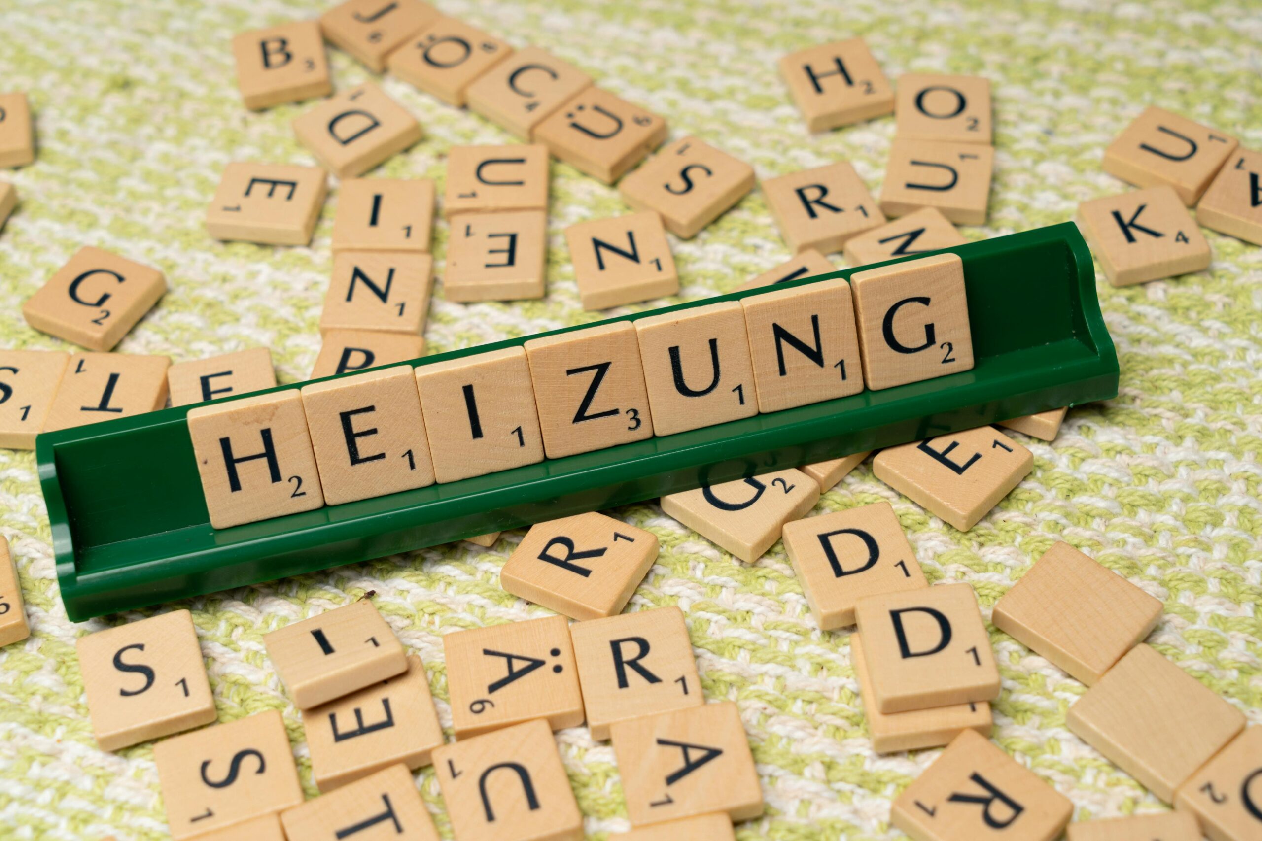 Close-up of wooden Scrabble tiles forming the word 'HEIZUNG' on a textured surface.